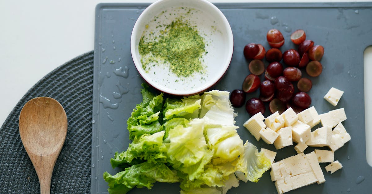 Fresh lettuce, grapes, and tofu with seasoning on a cutting board for a healthy meal preparation.