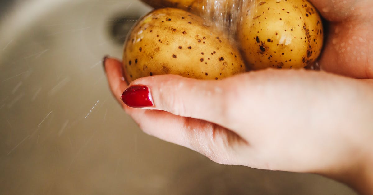 Hands washing fresh potatoes under water in kitchen sink, emphasizing cleanliness and nutrition.