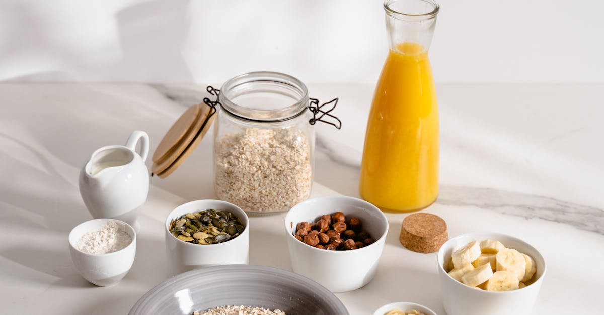 Flat lay of wholesome breakfast ingredients including oatmeal, nuts, banana, pumpkin seeds, and juice on a white surface.