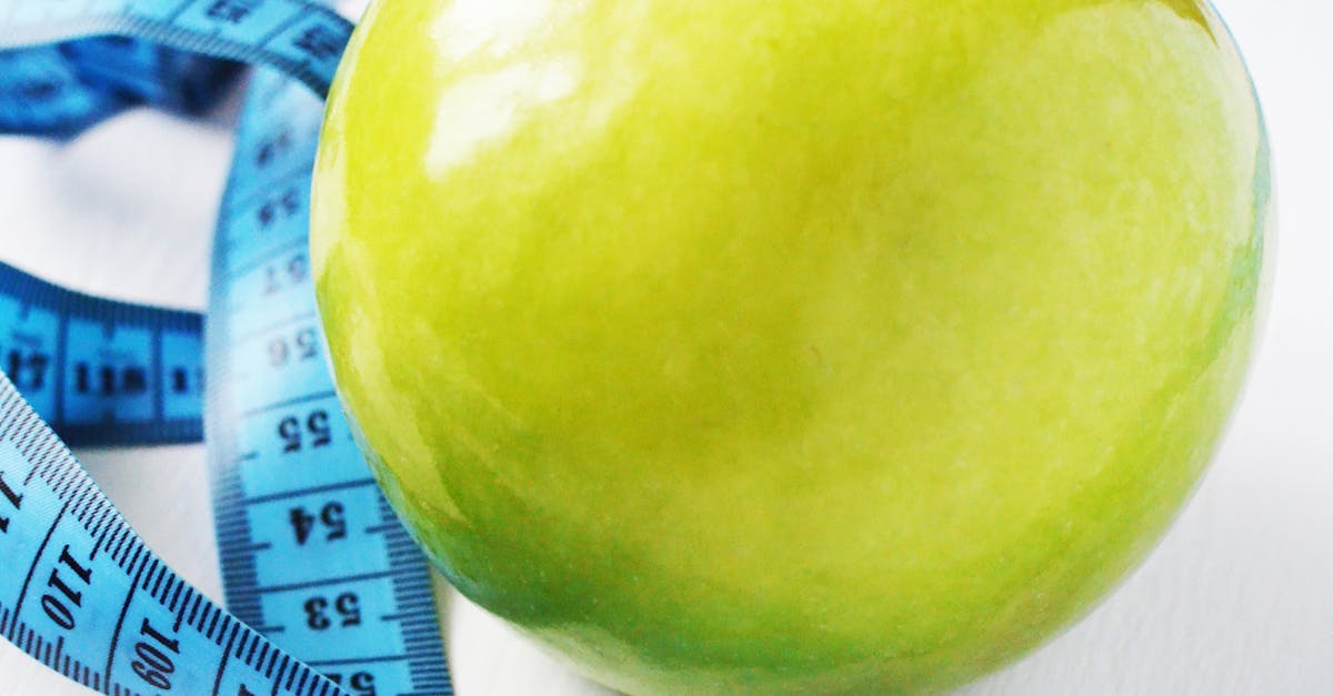 A fresh green apple surrounded by a blue measuring tape on a white background, symbolizing health and diet.